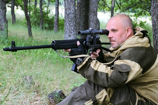 一个猎人拿着枪坐在森林里的树下瞄准目标