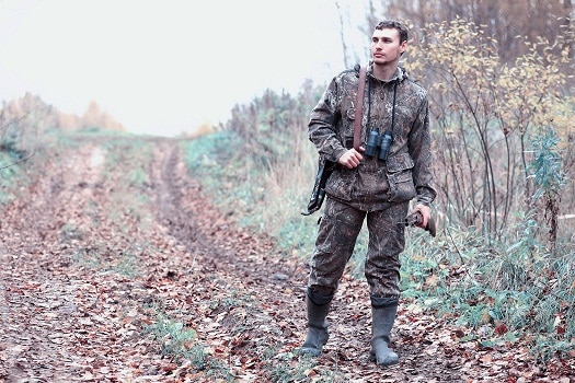 身着迷彩服，手持猎枪的男子在森林里进行春季狩猎