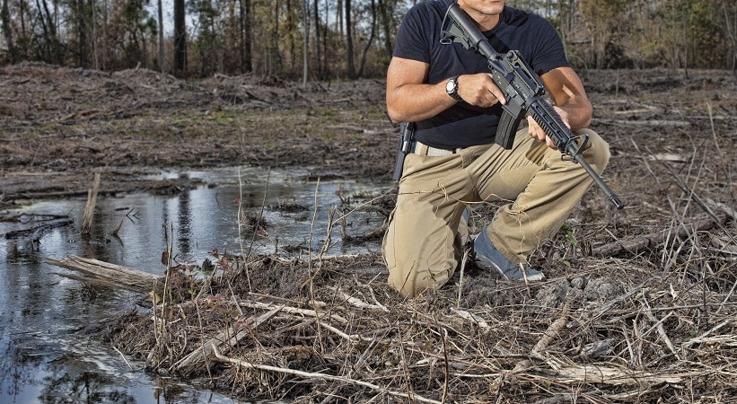 一个拿着AR-15的男人跪在水坑旁