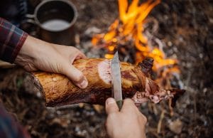 男子在森林营地雕刻烤兔肉