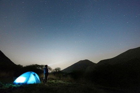 男人站在点燃的帐篷旁凝视星空