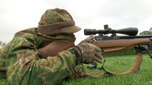 猎人在草地上用瞄准镜瞄准步枪