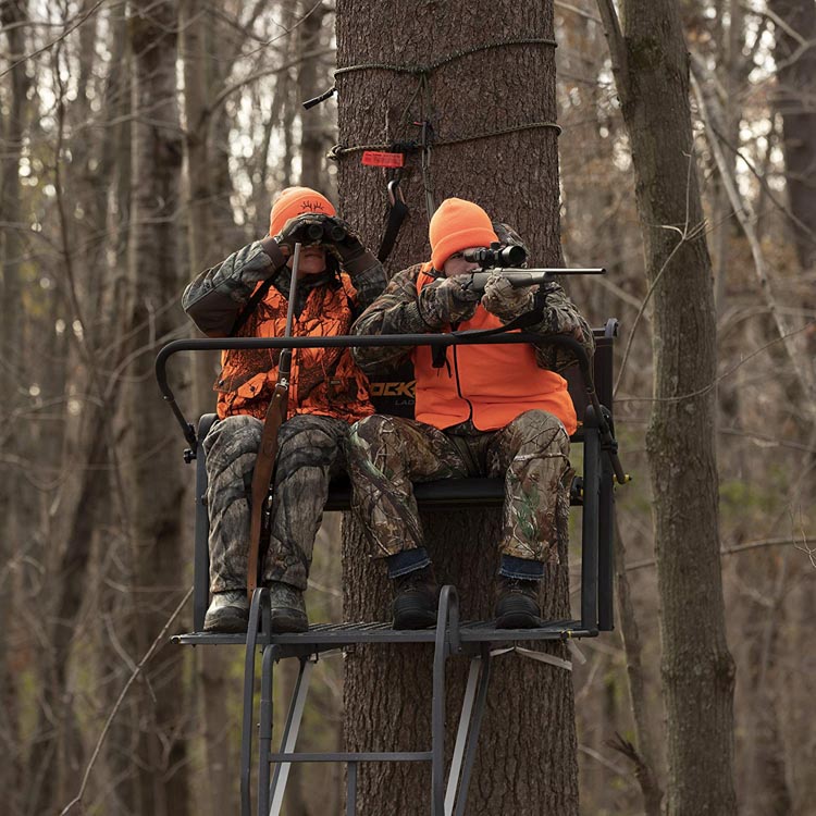 两个人坐在树林子里打猎，一个拿着双筒望远镜，一个拿着瞄准步枪