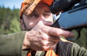 hunter in orange hat aiming rifle