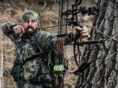 Hunter in camo drawing bow and aiming for clean shot behind a tree