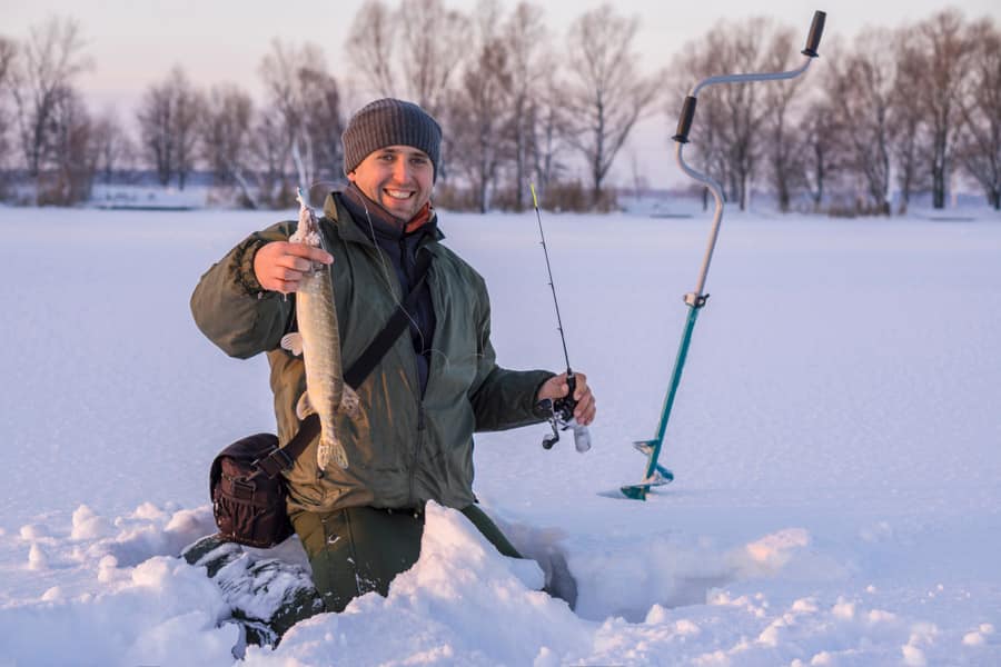 冬季钓鱼概念。渔夫在行动，手里拿着奖杯。在冰湖上捕梭鱼。