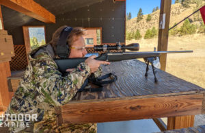 男子在狩猎迷彩测距距离与步枪瞄准镜坐在枪靶场板凳