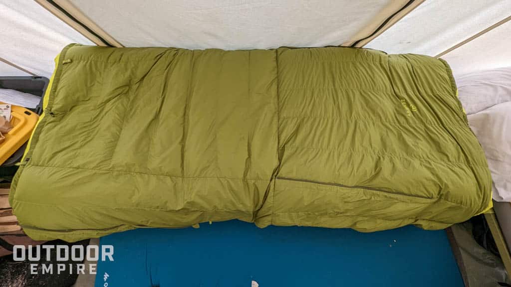 绿色的背包被子躺在床上的一个小床在一个炎热的帐篷在冬天露营