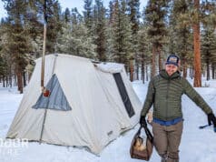 男子携带一个手提包柴火在炎热的帐篷前面的雪在冬天露营
