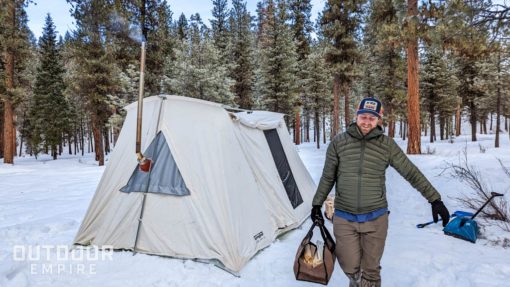 男子携带一个手提包柴火在炎热的帐篷前面的雪在冬天露营